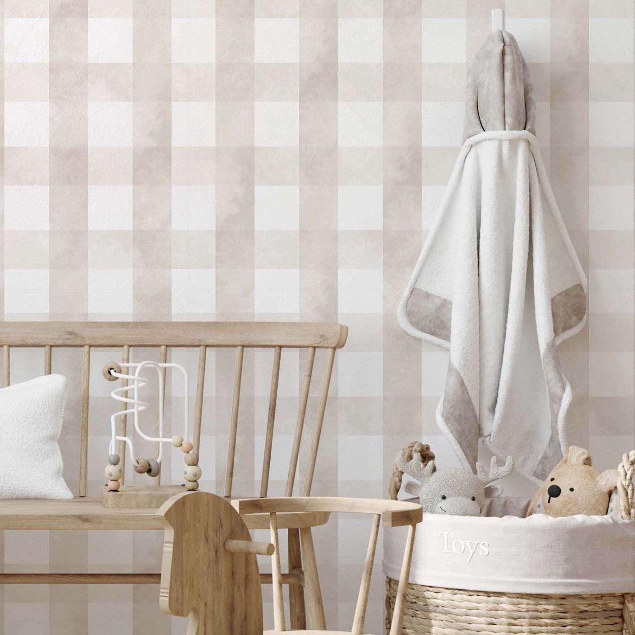 A cozy, neutral-toned nursery corner featuring light wood furniture, including a bench and a small rocking horse. A woven basket holds plush animals, and a soft hooded towel hangs on the wall. The backdrop is a soft beige checkered wallpaper, adding a subtle pattern to the space.