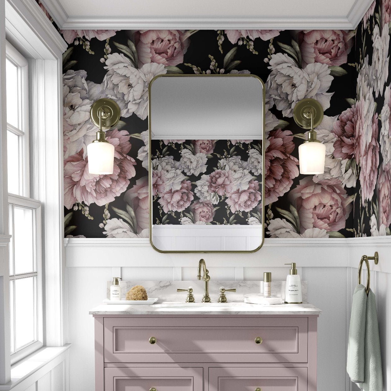 Bathroom with a bold pink and white peony floral wallpaper, featuring large flowers against a dark background. A light pink vanity with gold fixtures stands below a rectangular mirror with rounded edges, flanked by brass sconces with globe lights. The space has an elegant, vintage feel, with white paneling beneath the wallpaper and a window to the left allowing natural light.