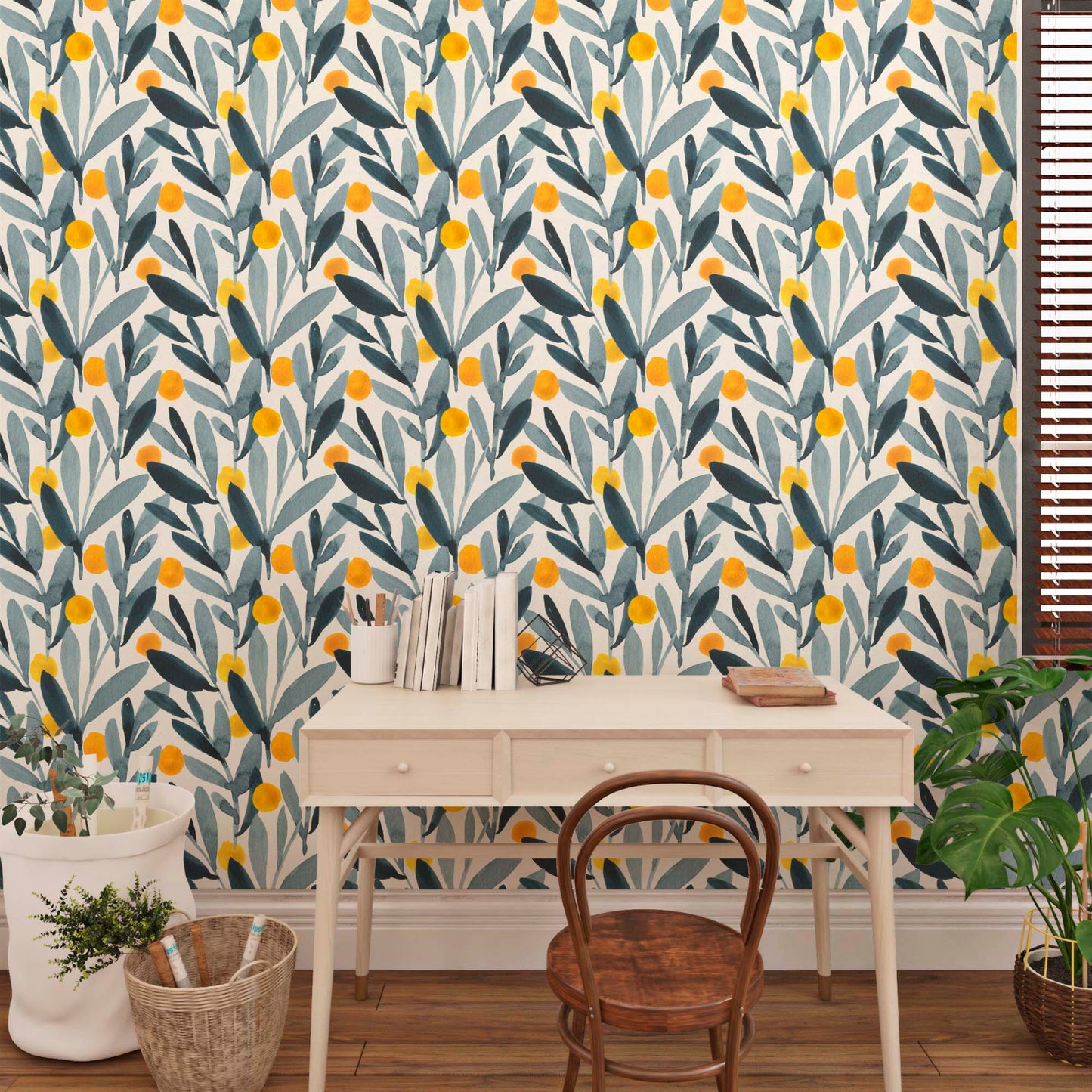 A desk with books and a chair in front of a colorful leaf-patterned wallpaper, next to a window with blinds and a potted plant.