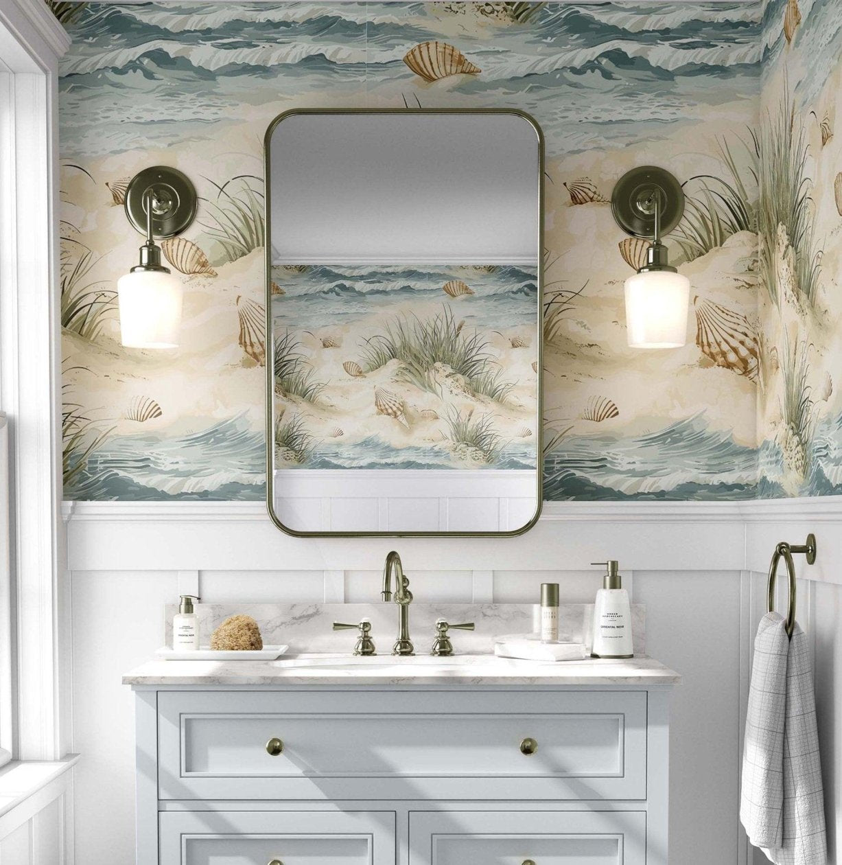 A tranquil bathroom showcasing a colorful mural of a beach and seashells on the wall, enhancing the coastal ambiance, a light grey vanity with gold accents. A large rectangular mirror with rounded edges hangs above the vanity, flanked by two brass sconces with white globe lights.
