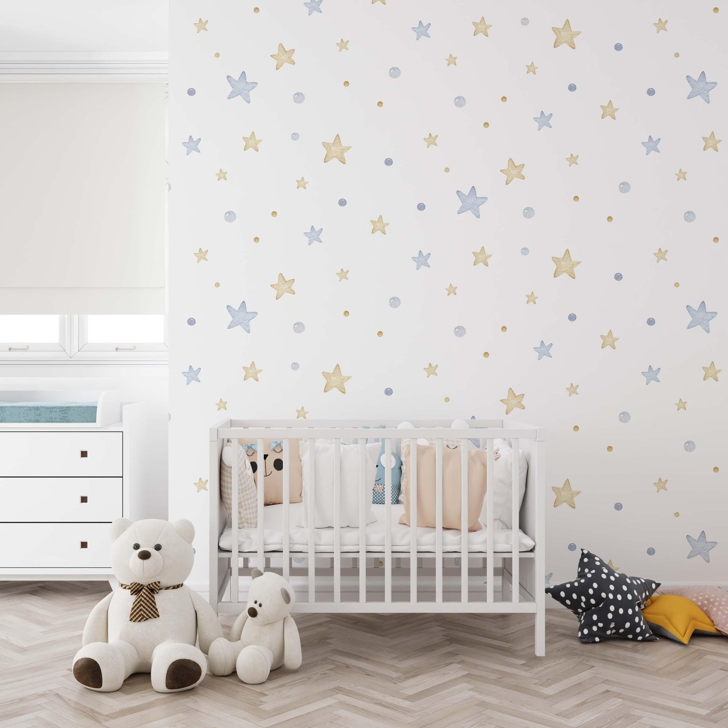 Modern nursery with starry wallpaper in pastel blue and gold. The space includes a white crib with white, beige and pale blue cushions and a white chesto of drawers.