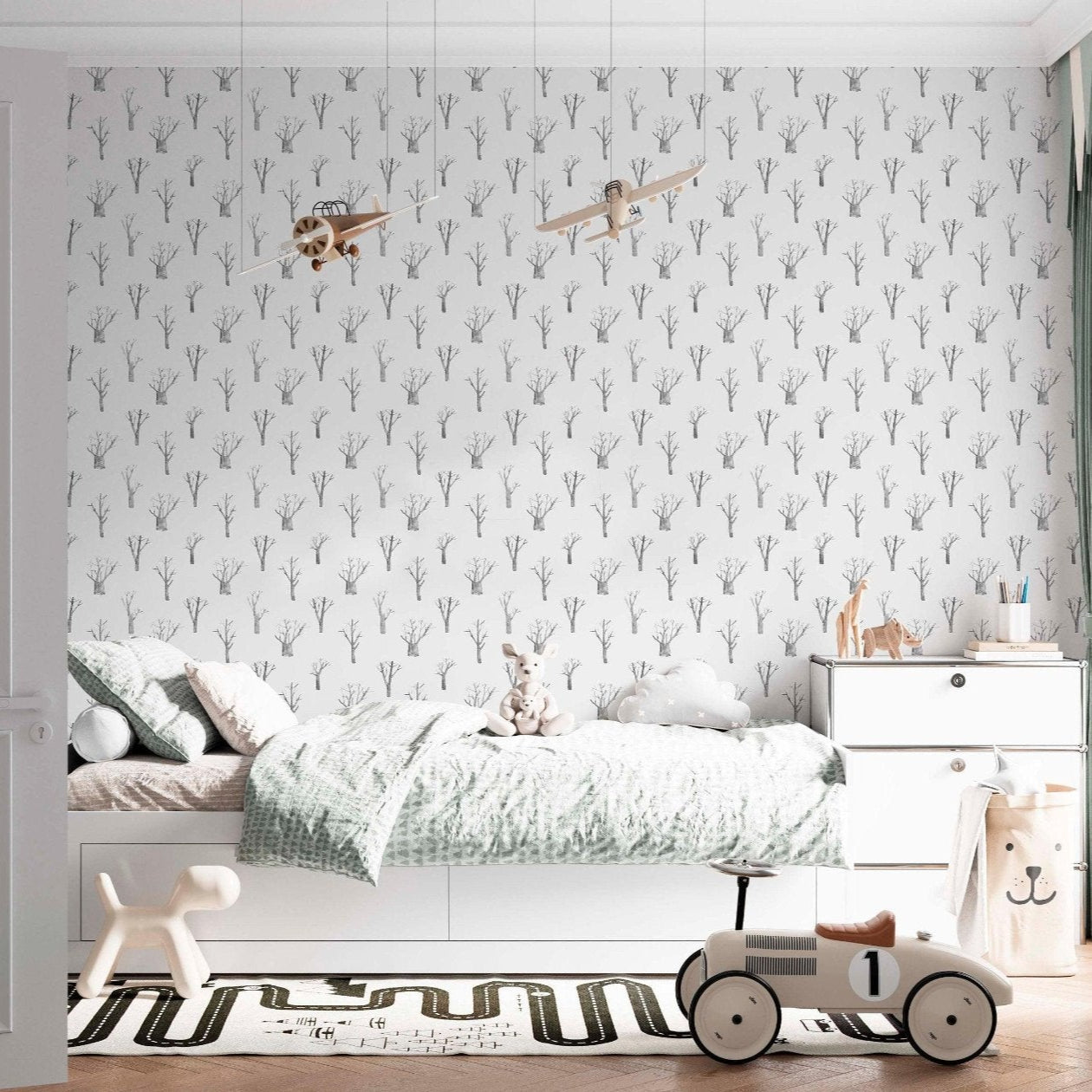 A bedroom with a bed and toys and a wallpaper with grey trees and a white background