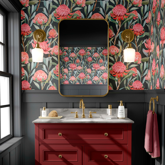 Modern bathroom with red floral wallpaper on a charcoal background, gold-framed mirror, red vanity, and brass fixtures on a marble countertop.
