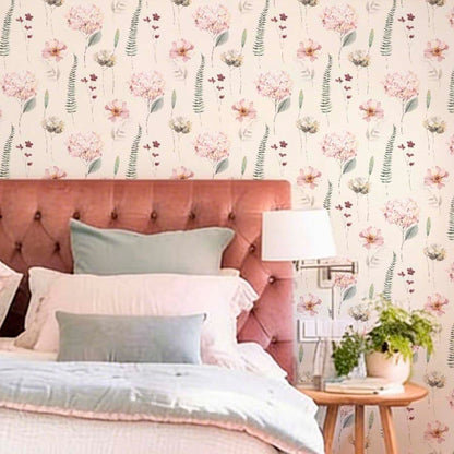 cat-616983200072 A bed with a pink tufted headboard and blue-grey pillows set against a floral hydrangea watercolor wallpaper. A wooden side table with a lamp and plant stands nearby.
