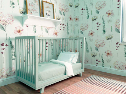 A close-up of a nursery corner with a grey crib and white linens. The Hydrangea watercolor wallpaper provides a soft backdrop with its floral design.