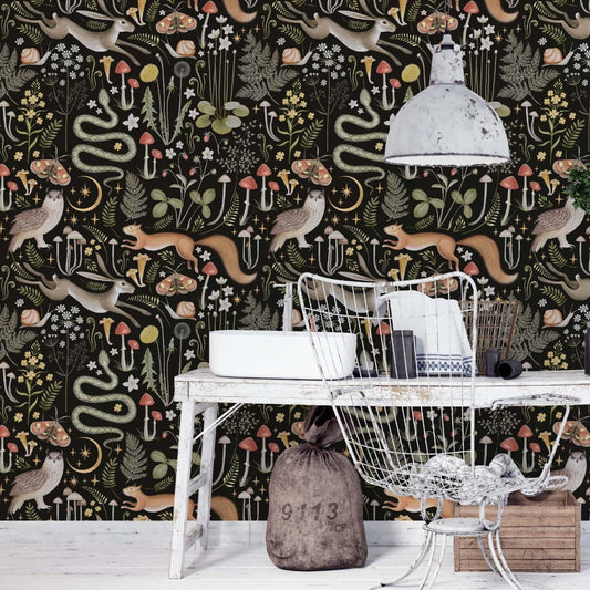 Room with rustic decor and a moody atmosphere, featuring a white table, wire chair, hanging metal lamp, and wallpaper with nature motifs—squirrels, snakes, and mushrooms—perfect for those who appreciate the cottagecore aesthetic.