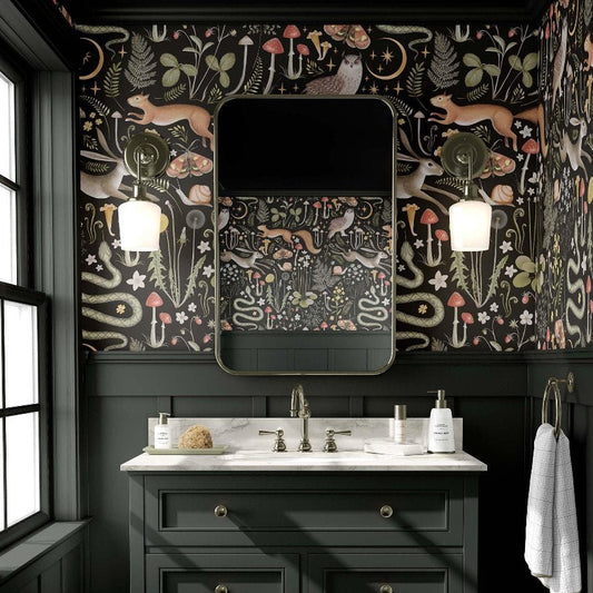 cat-610804236616 A moody powder room features black and floral patterned wallpaper, a dark green vanity with a white countertop, and a rectangular mirror flanked by lights above the sink, creating an ambiance inspired by nature.