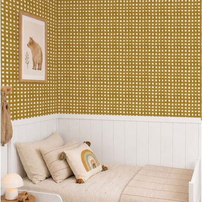 Mustard hand painted grid wallpaper in a Scandinavian children's bedroom with white wainscoting, natural wood details and soft neutral bedding.