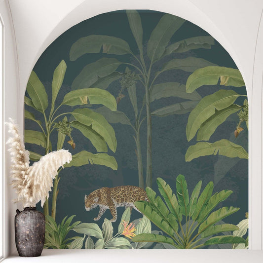 Illustration of a tropical jungle scene framed by a white architectural arch, featuring large banana leaves, dense greenery, and a spotted leopard walking through the foliage. A dark ceramic vase with pampas grass sits in the foreground, creating a calm, elegant interior design setting.