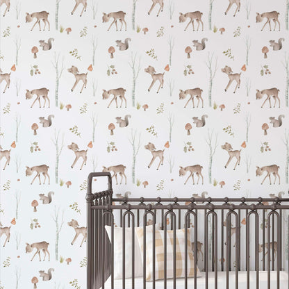 Nursery wall with woodland-themed wallpaper featuring illustrated fawns, squirrels, mushrooms, and birch trees, seen behind a dark metal spindle crib with a checkered pillow.