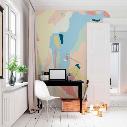Creative home office workspace featuring a large abstract pastel wall mural behind a black desk with a white chair and floor candles.
