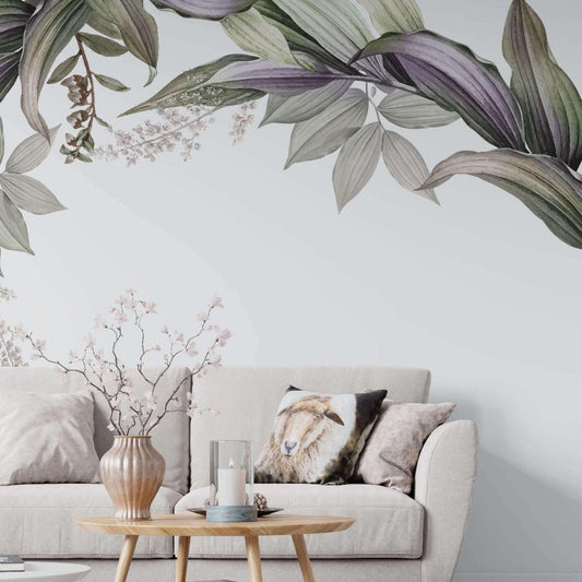 A botanical wallpaper mural with large green and purple leaves on white background in a living room with cream sofa and light wood coffee table