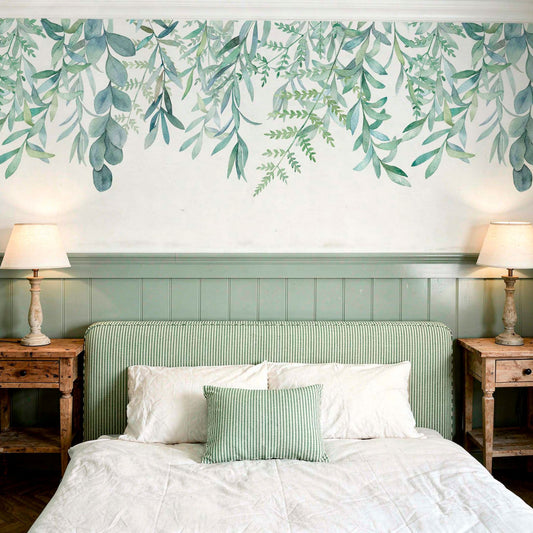 Hanging leaves wallpaper mural with watercolour eucalyptus and botanical leaves in sage green above a bed with striped headboard and rustic wood nightstands