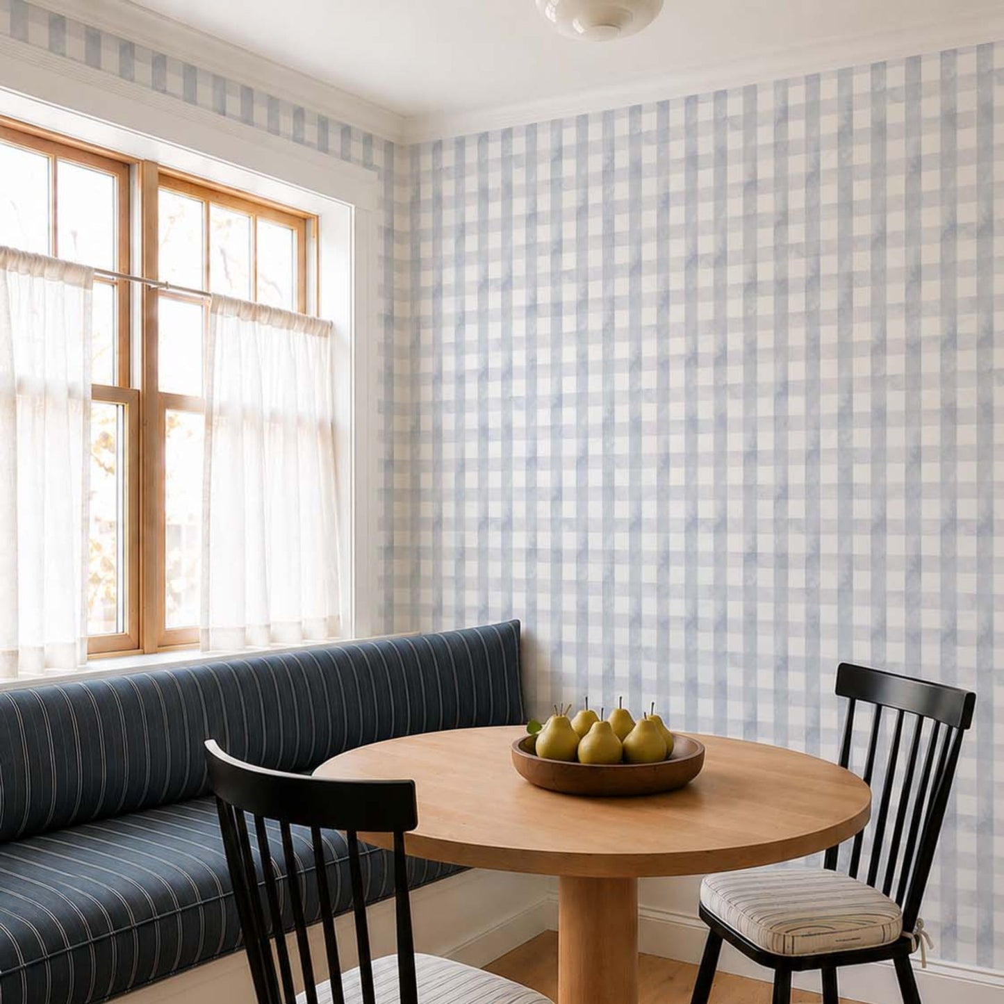 cat-659356549448 Blue grey gingham wallpaper in a cozy breakfast nook with a built-in upholstered bench, round oak table, black Windsor chairs and soft natural light.