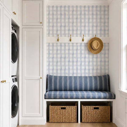cat-615198490952 Blue grey gingham wallpaper in a bright mudroom with built-in bench seating, hidden laundry cabinets, white shaker cabinetry and woven storage baskets.