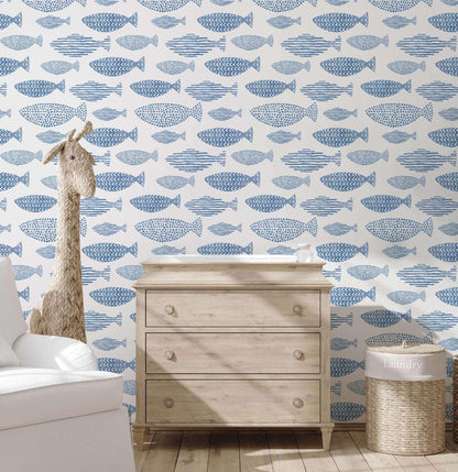 A children's room with blue fish-themed wallpaper and a wooden chest of drawers.