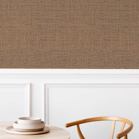 cat-659356549448   A close-up of a dining area featuring brown burlap-textured wallpaper on the upper half of the wall. Below a white chair rail, there is classic white paneled wainscoting. In the foreground, a light wood dining table holds three stacked beige ceramic bowls, and the curved wooden back of a chair is partially visible.
