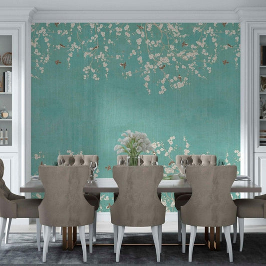 cat-610512830792 Elegant dining room with a teal Chinoiserie wallpaper mural featuring delicate pink cherry blossoms, surrounded by white built-in bookshelves and grey tufted chairs.