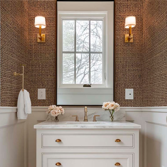 Elegant small bathroom featuring a focal wall with dark brown grasscloth-textured wallpaper. The textured wall is paired with classic white wainscoting, a marble-top vanity, and two gold-toned wall sconces flanking a central mirror.