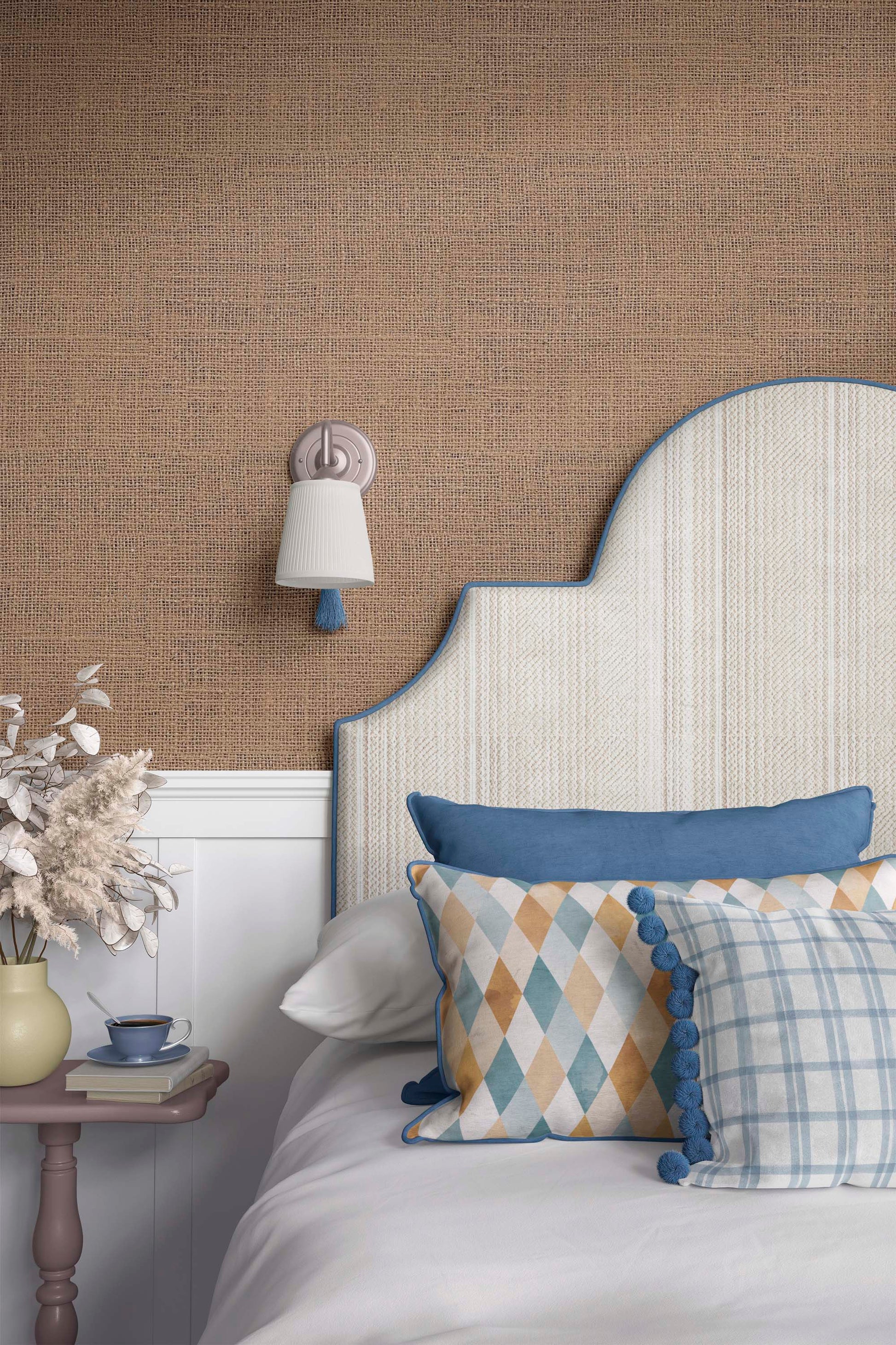 A cozy bedroom setup featuring a decorative headboard with a blue trim, patterned pillows on a white bed, a bedside table with a small cup and decorative flowers, and a soft light fixture on the wall against a textured brown background.