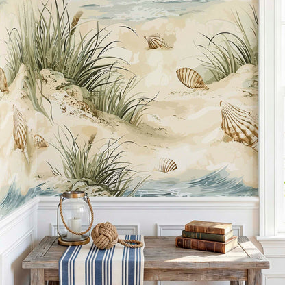 cat-610569683272 Nautical wallpaper mural with seashells and beach grass on a wall above a rustic wooden table with decorative coastal items.