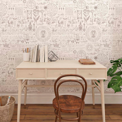 cat-610804433224 A minimalist wooden desk and vintage chair against a wall with apothecary and alchemist manuscript wallpaper, featuring botanical sketches, sun symbols, and Latin tex