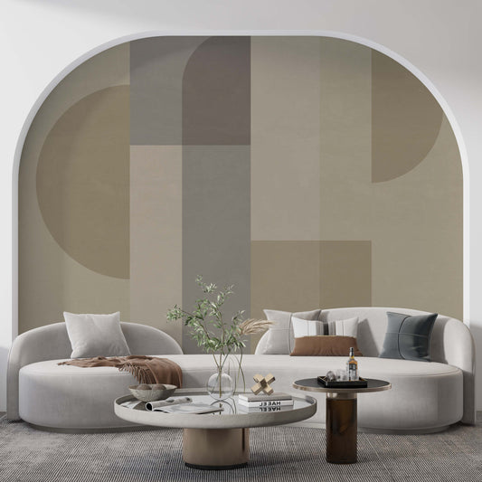 A contemporary living room featuring a large arched wall mural with abstract geometric shapes in shades of beige, taupe, and muted green. In front of the mural is a curved, low-profile cream sofa with various decorative pillows. Two round coffee tables of different heights sit on a textured grey rug.