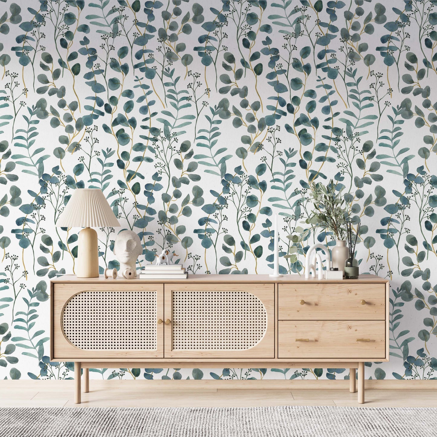  cat- 659356549448A bright living space featuring a teal and white botanical wallpaper with watercolor eucalyptus leaves. A modern light wood sideboard with rattan doors is centered against the accent wall, decorated with a pleated table lamp, minimalist sculptures, and a vase with greenery. The room has a clean, Scandinavian-inspired aesthetic with light flooring and a textured gray rug.