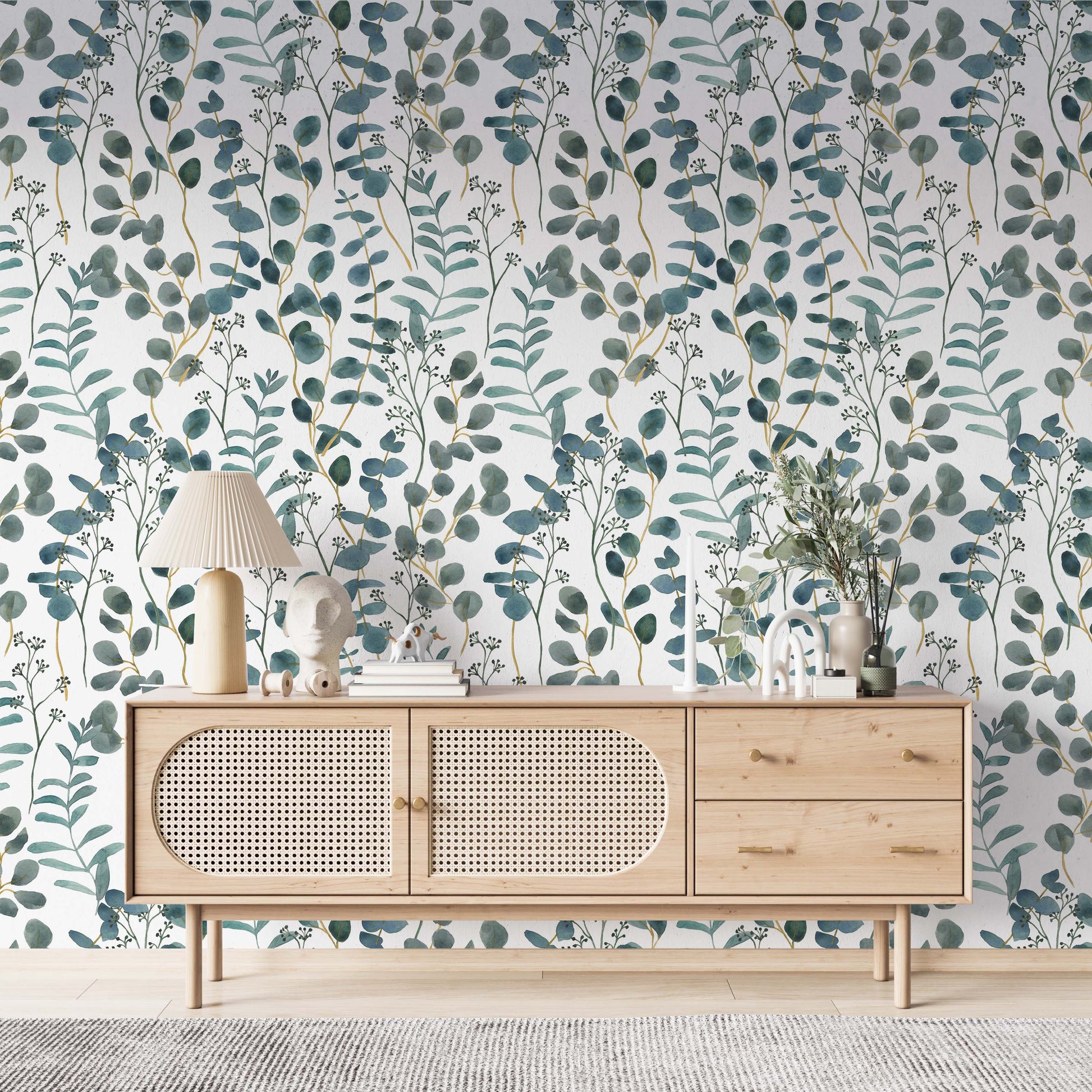  cat- 659356549448A bright living space featuring a teal and white botanical wallpaper with watercolor eucalyptus leaves. A modern light wood sideboard with rattan doors is centered against the accent wall, decorated with a pleated table lamp, minimalist sculptures, and a vase with greenery. The room has a clean, Scandinavian-inspired aesthetic with light flooring and a textured gray rug.