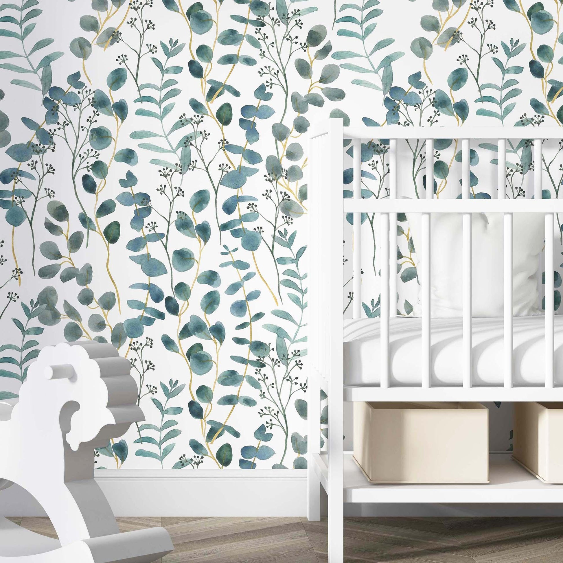 cat-615198294344 A bright nursery featuring a teal and white botanical wallpaper with watercolor eucalyptus leaves as an accent wall. A white wooden crib with neutral storage bins underneath is positioned against the wall, accompanied by a white wooden rocking horse in the foreground. The room has light wood flooring, creating a calm and modern aesthetic for a baby's room.