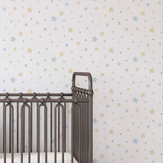A close-up of a dark brown metal baby crib against a white nursery wall with a repeating pattern of light blue and gold watercolor stars and dots.