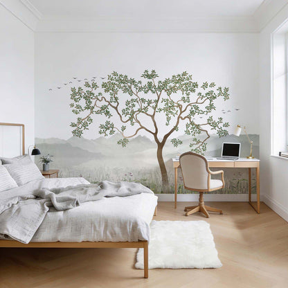  A bedroom and home office space featuring a large wall mural wallpaper with a central green tree, misty watercolor mountains, and flying birds.