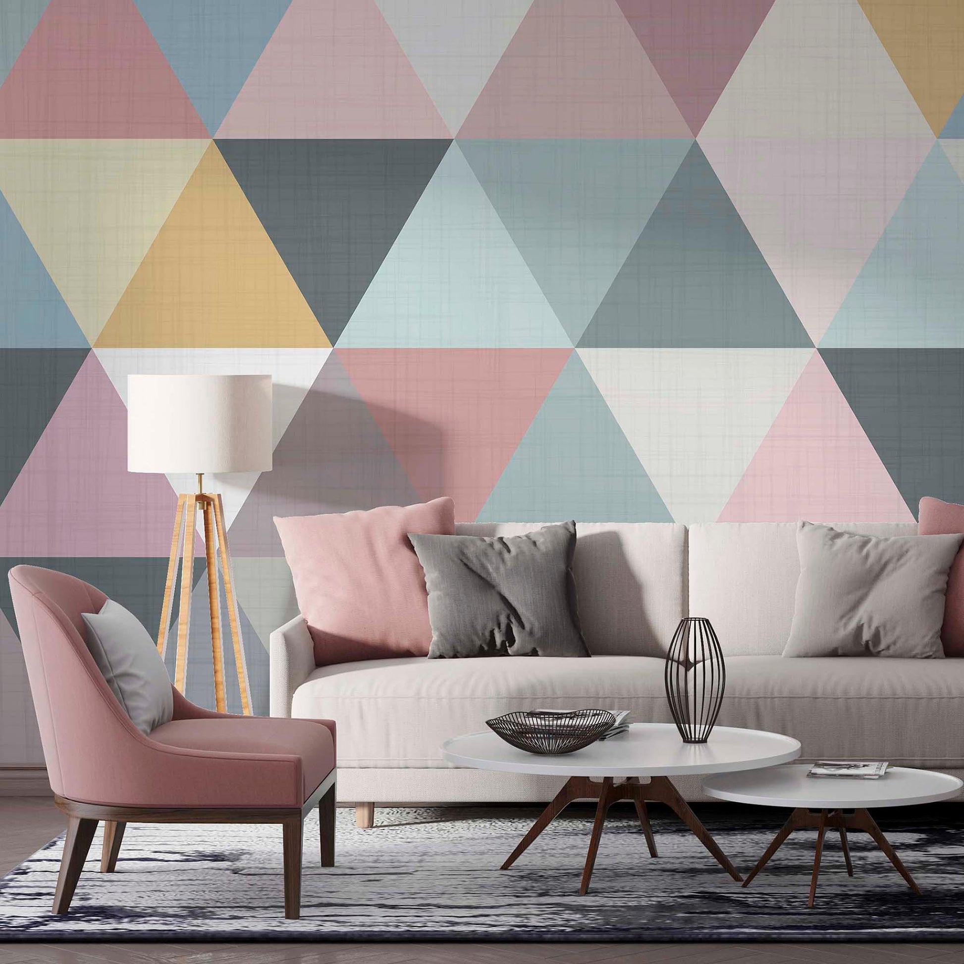 cat-610569683272  A modern living room featuring a pastel geometric triangle wallpaper mural behind a cream sofa with pink and grey pillows, a dusty pink armchair, and a white coffee table.