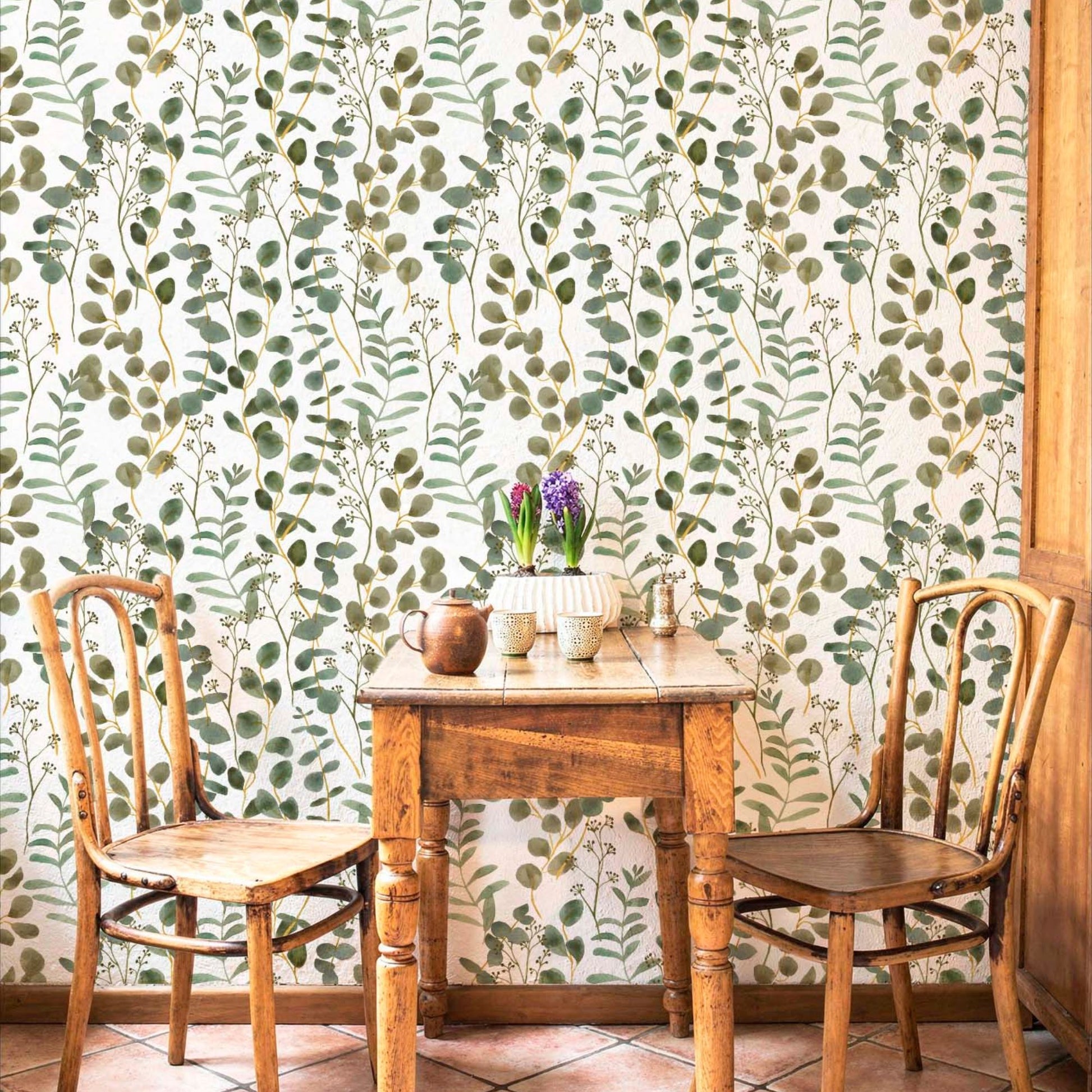 cat- 659356549448 Rustic dining nook featuring green eucalyptus watercolor wallpaper, a vintage wooden table, and two classic wooden chairs.
