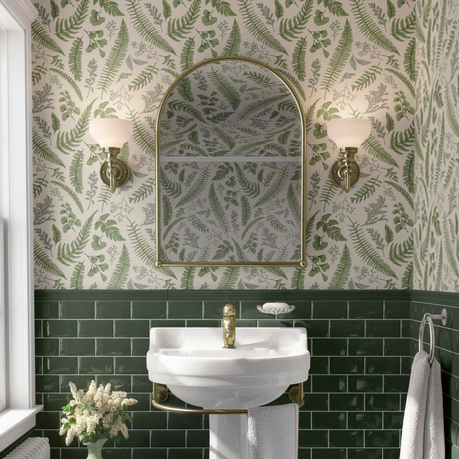 cat-610804236616 A luminous and classic bathroom featuring a lush botanical wallpaper with vibrant green fern fronds and delicate leaves on a white background. The pattern extends across the upper walls and ceiling, beautifully paired with deep emerald green subway tiles on the lower half. A white pedestal sink with brass fixtures is centered below an arched gold-framed mirror, flanked by elegant traditional wall sconces, creating a refreshing nature-inspired sanctuary.