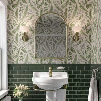cat-610804236616 A luminous and classic bathroom featuring a lush botanical wallpaper with vibrant green fern fronds and delicate leaves on a white background. The pattern extends across the upper walls and ceiling, beautifully paired with deep emerald green subway tiles on the lower half. A white pedestal sink with brass fixtures is centered below an arched gold-framed mirror, flanked by elegant traditional wall sconces, creating a refreshing nature-inspired sanctuary.