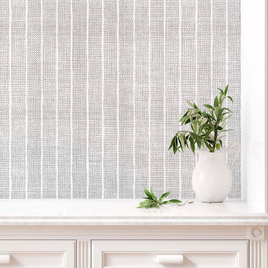 cat-659356549448 Close-up of a grey and white textured stripe wallpaper above a white marble countertop with a white ceramic pitcher holding olive branches.