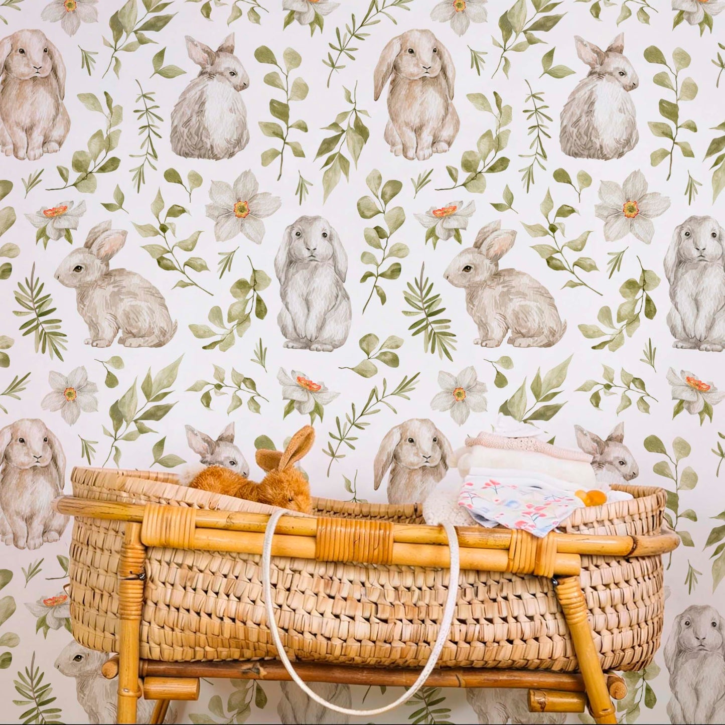 Hand-painted wallpaper featuring brown bunnies, delicate green leaves, and soft white flowers behind a woven wicker bassinet.