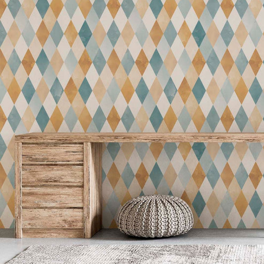 cat-610804433224 Geometric harlequin wallpaper with a watercolor diamond pattern in blue, ochre, and beige tones behind a rustic wooden desk and a knitted floor pouf in a home office.