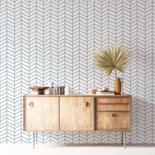Hand-drawn herringbone wallpaper in teal and white, featured on a living room wall behind a mid-century modern wooden sideboard with decorative gold bowls and a dried palm leaf.