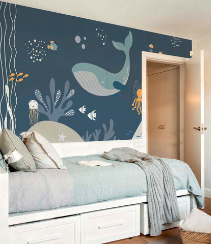 cat-661212758344  Decorative kids wallpaper featuring an illustrated dark blue underwater scene with whales behind a white trundle bed with light blue and grey bedding.
