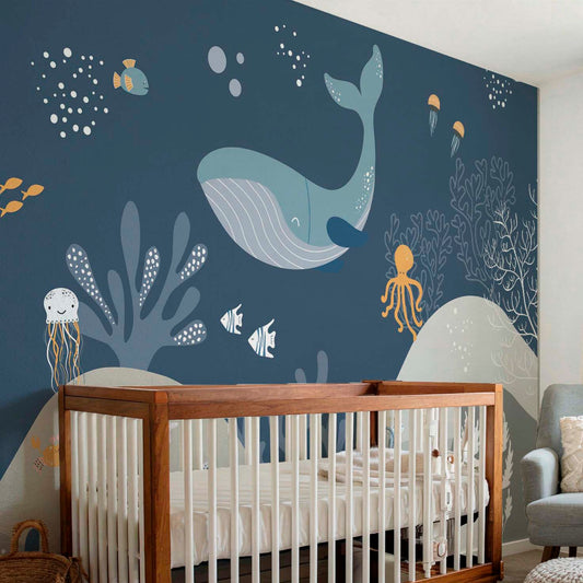 Decorative kids wallpaper featuring an illustrated dark blue underwater scene with a large whale behind a natural wood crib in a modern baby nursery.