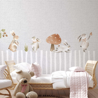 Decorative kids wallpaper featuring watercolor forest bunnies over a grey faux linen textured striped background on a bedroom wall behind a natural rattan toddler bed with a large teddy bear.