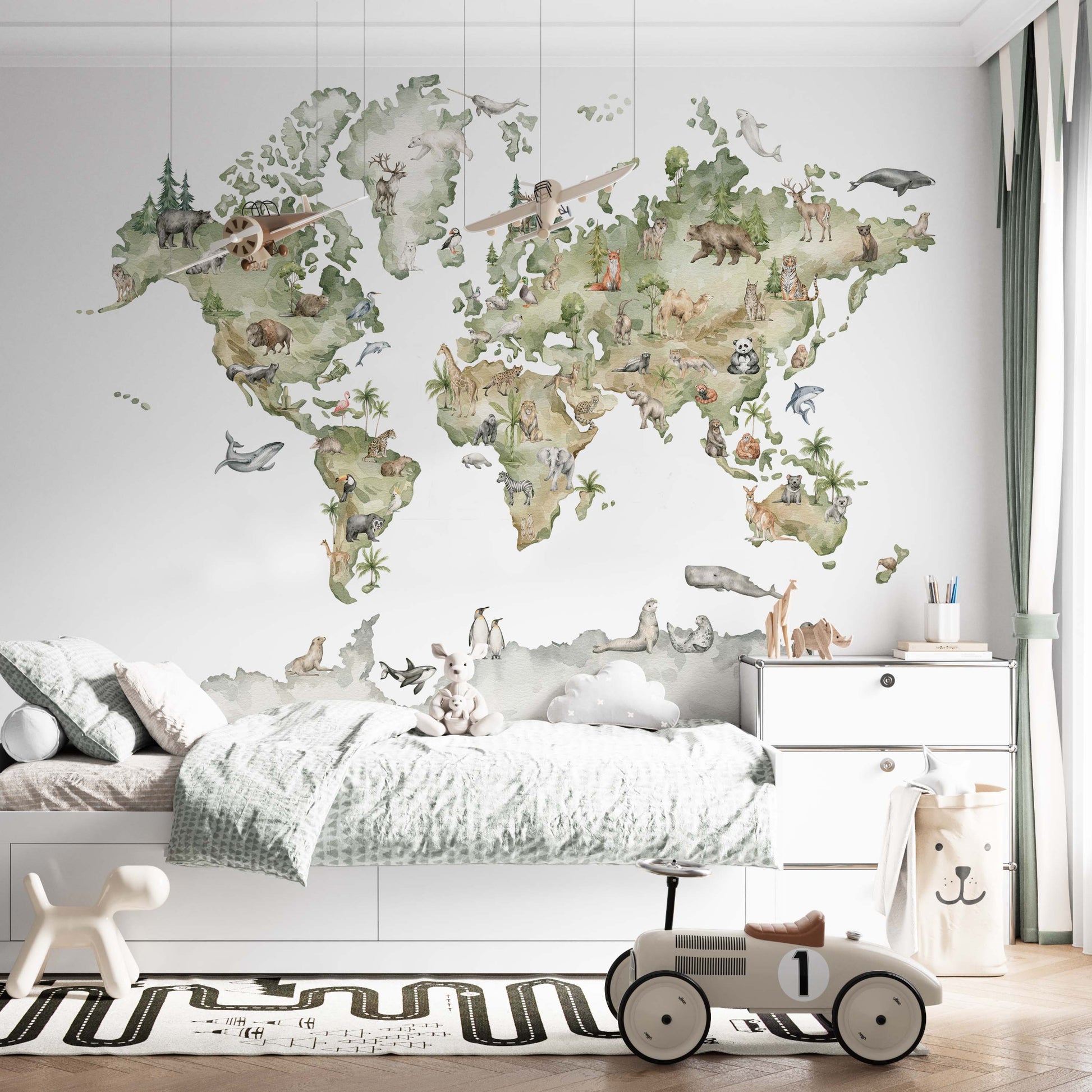 cat-661212758344 Gender-neutral world map wallpaper with safari and arctic animals on a kids' bedroom wall behind a white bed with a classic toy ride-on car.