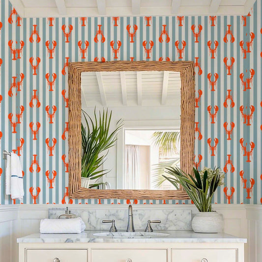 Coastal bathroom interior featuring lobster and blue striped wallpaper with a wicker mirror and marble countertop.
