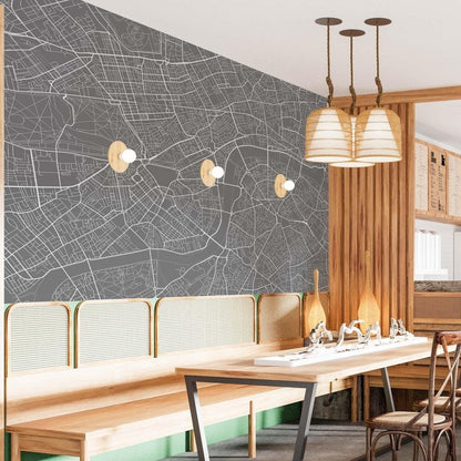 cat-610512830792 London street map mural wallpaper in dark grey and white in a dining room with wooden table, rattan chairs and pendant lights