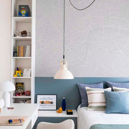 London street map mural wallpaper in light grey in a teen bedroom with white bed, blue cushions and built-in bookshelf