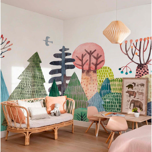 Magical forest kids mural wallpaper in a playroom with rattan sofa and pink chairs, colorful illustrated trees and birds in watercolor style