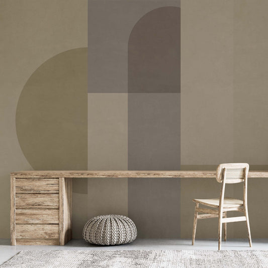 cat-660961526088 A minimalist home office featuring a long light-wood desk with a built-in chest of drawers and a vintage-style cane back chair. The focal point is a large-scale geometric wall mural with overlapping circles and arches in muted earth tones of sage green, taupe, and brown. A grey knitted pouf sits under the desk on a textured grey rug