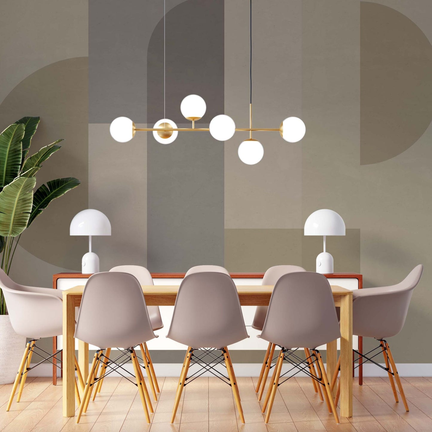 cat-610512830792 A modern dining room featuring a wooden table surrounded by six light grey Eames-style chairs with wooden legs. A brass linear chandelier with six white globe bulbs hangs above the table. The background features a large-scale geometric wall mural in muted earth tones of sage, taupe, and beige, with two white mushroom-style table lamps sitting on a side console